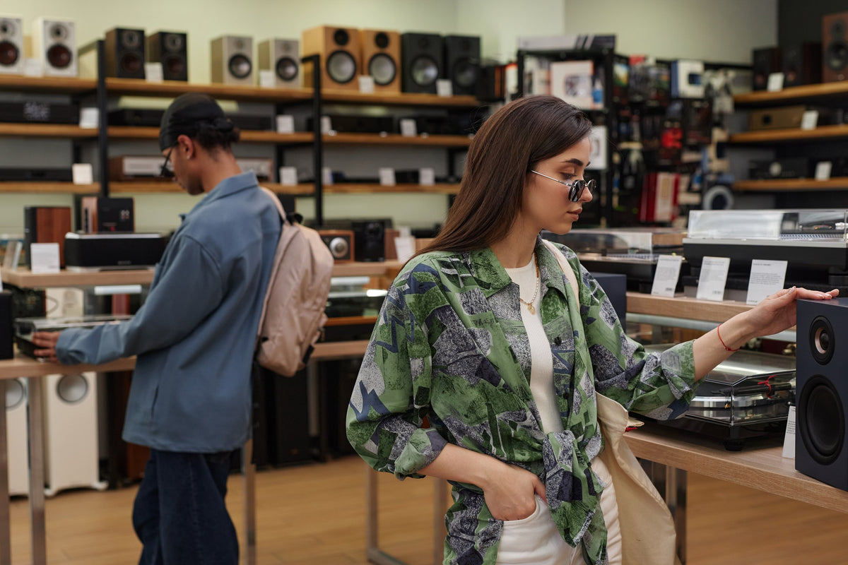 Two customers browsing hi-fi speakers and turntables in an audio specialist showroom